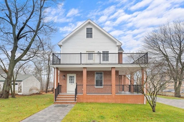 view of front of home featuring brick siding, a front lawn, a balcony, and covered porch