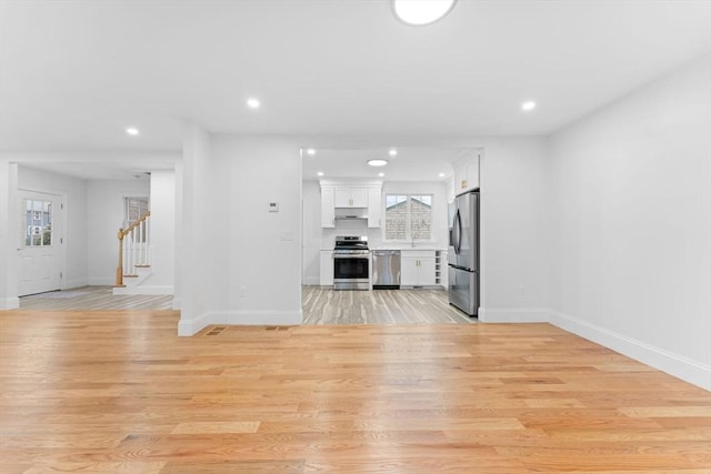 unfurnished living room with recessed lighting, baseboards, light wood finished floors, and stairway