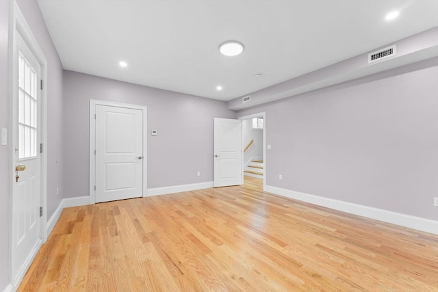 empty room with light wood-style floors, baseboards, stairs, and visible vents