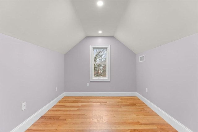 additional living space with baseboards, vaulted ceiling, light wood finished floors, and visible vents