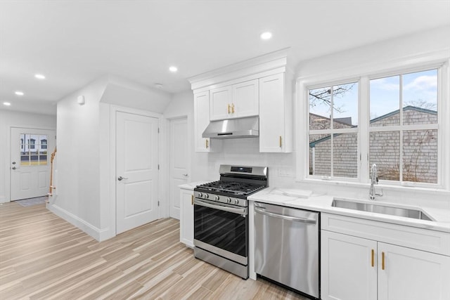 kitchen with white cabinetry, under cabinet range hood, a sink, light wood finished floors, and appliances with stainless steel finishes