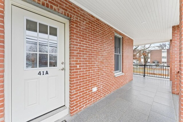 doorway to property with covered porch and brick siding