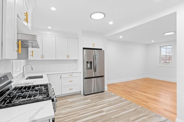 kitchen featuring appliances with stainless steel finishes, light stone counters, a sink, white cabinetry, and baseboards
