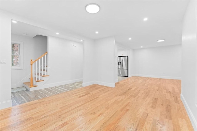 basement featuring stairs, baseboards, stainless steel fridge with ice dispenser, and light wood-type flooring