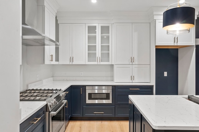 kitchen with light stone counters, wall chimney exhaust hood, decorative light fixtures, white cabinets, and stainless steel stove