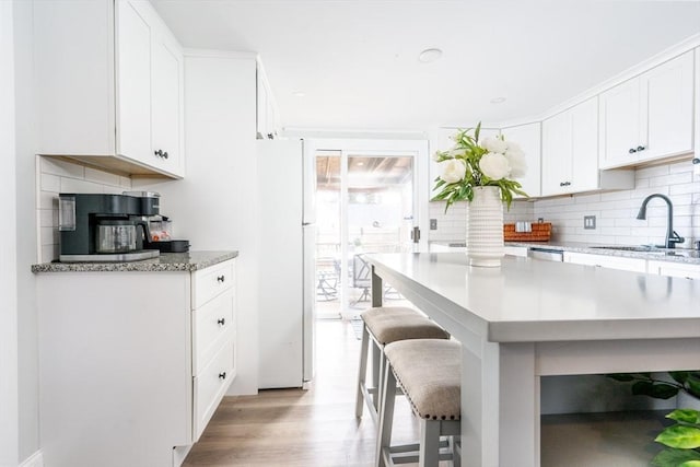 kitchen with a breakfast bar, sink, white cabinetry, light hardwood / wood-style floors, and decorative backsplash