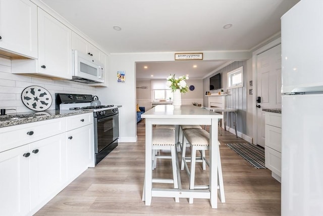 kitchen with a breakfast bar area, white cabinetry, white appliances, light stone countertops, and decorative backsplash