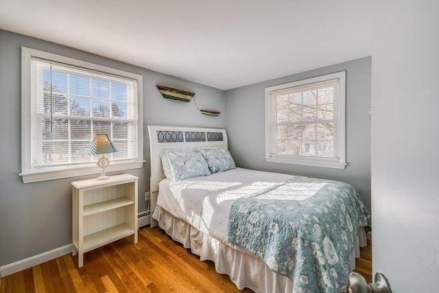 bedroom featuring multiple windows, hardwood / wood-style flooring, and baseboard heating