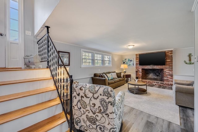 living room featuring hardwood / wood-style flooring, ornamental molding, and a brick fireplace