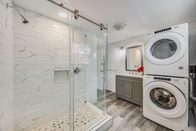 bathroom with walk in shower, stacked washer / drying machine, wood-type flooring, and vanity