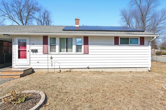 ranch-style house featuring roof mounted solar panels and a chimney