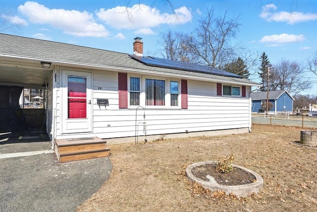 view of front of home with roof with shingles, solar panels, a chimney, and fence