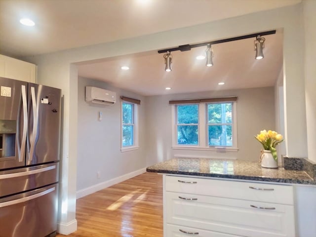 kitchen featuring light wood-type flooring, dark stone counters, an AC wall unit, white cabinets, and stainless steel fridge with ice dispenser