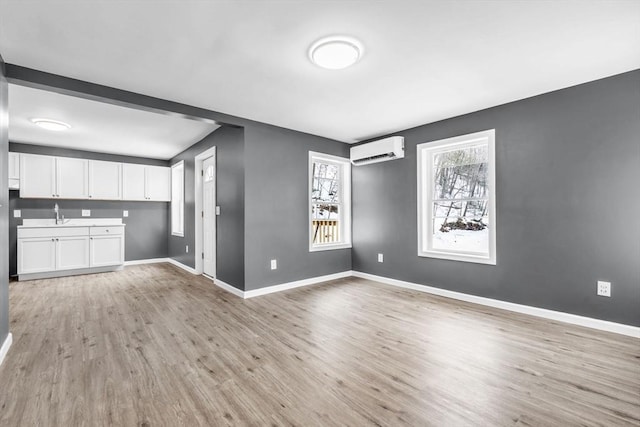 unfurnished living room with a sink, light wood-style flooring, baseboards, and a wall mounted AC