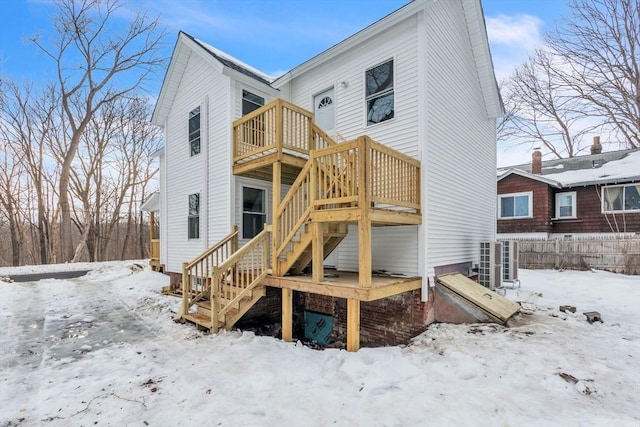 snow covered house with stairway and a wooden deck