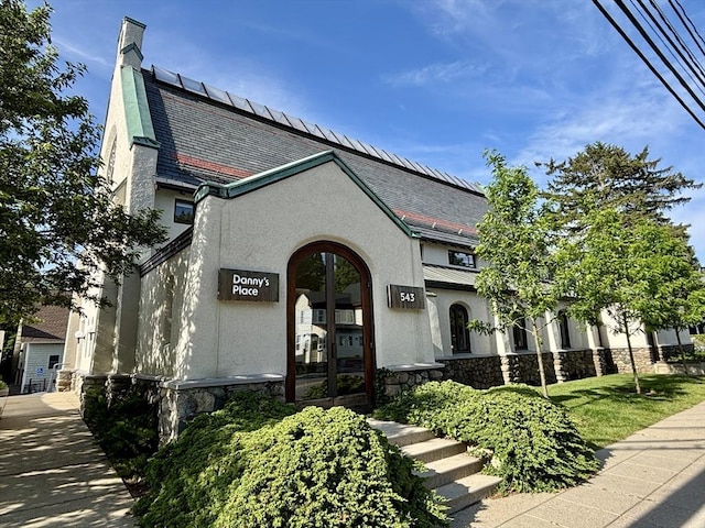 250 Arlington St Unit A, Acton, MA 01720 - view of front facade with stucco siding, roof mounted solar panels, stone siding, and a high end roof