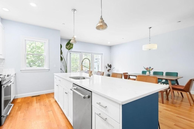 kitchen with appliances with stainless steel finishes, a sink, light wood finished floors, white cabinets, and recessed lighting