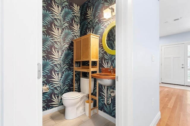 bathroom featuring wallpapered walls, baseboards, a sink, toilet, and an accent wall