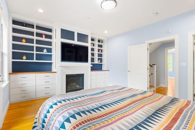 bedroom with light wood-type flooring, a glass covered fireplace, baseboards, and recessed lighting