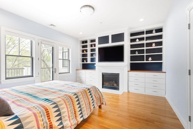 bedroom with light wood-type flooring, a glass covered fireplace, access to exterior, and baseboards