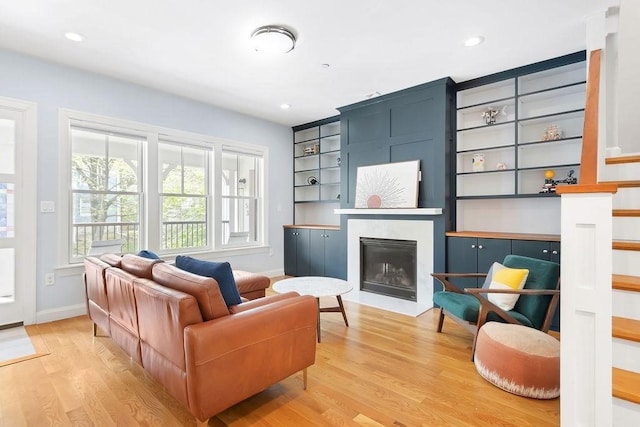 living area featuring light wood-type flooring, baseboards, a fireplace with flush hearth, recessed lighting, and built in shelves