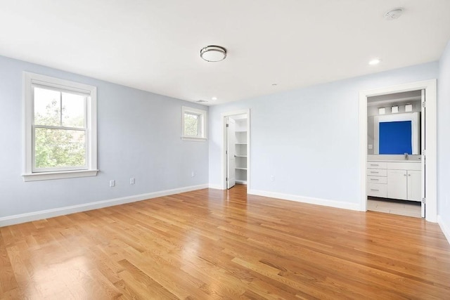 unfurnished bedroom with light wood-style flooring, baseboards, a spacious closet, a sink, and connected bathroom