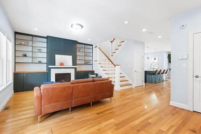 living area with a large fireplace, stairway, light wood finished floors, baseboards, and recessed lighting