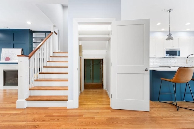 stairs with a glass covered fireplace, wood finished floors, and recessed lighting