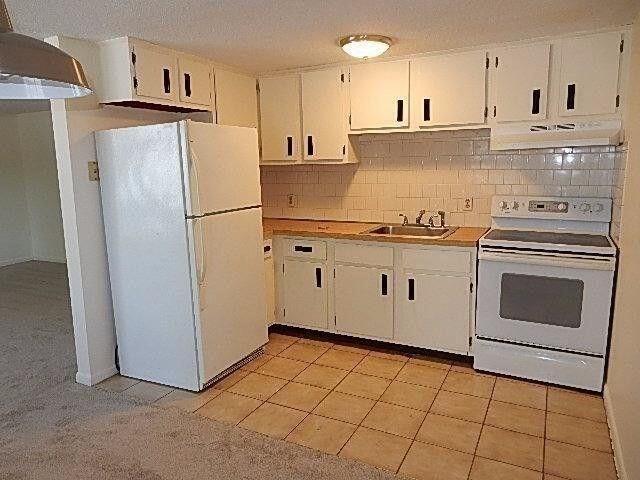 kitchen with white appliances, light countertops, white cabinetry, a sink, and exhaust hood