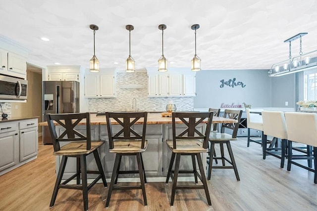 kitchen featuring white cabinets, decorative light fixtures, stainless steel appliances, backsplash, and light wood-type flooring