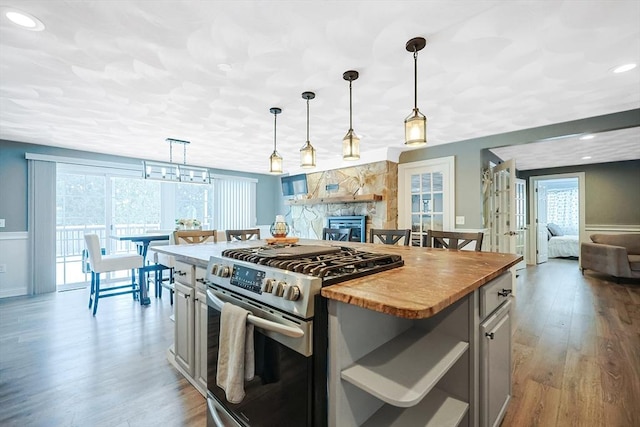 kitchen with a center island, stainless steel gas range, light hardwood / wood-style flooring, pendant lighting, and butcher block countertops