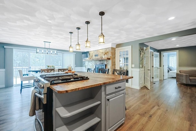 kitchen with pendant lighting, wooden counters, light wood-type flooring, a stone fireplace, and stainless steel gas range oven