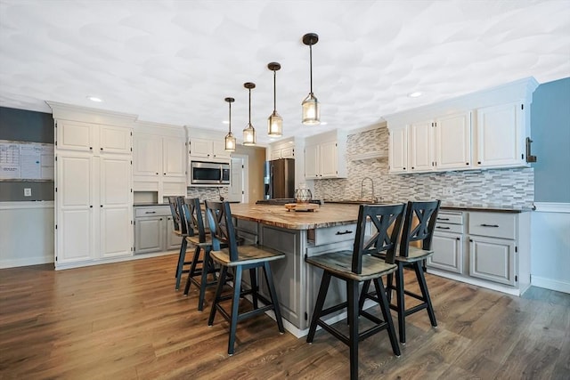 kitchen with a center island, appliances with stainless steel finishes, hanging light fixtures, white cabinets, and butcher block countertops