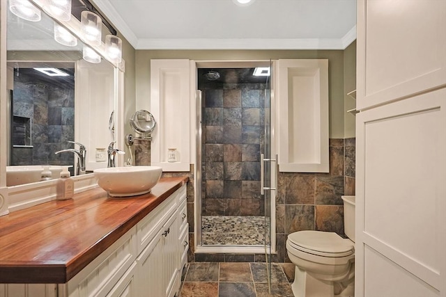 bathroom with a shower with shower door, toilet, crown molding, tile walls, and vanity