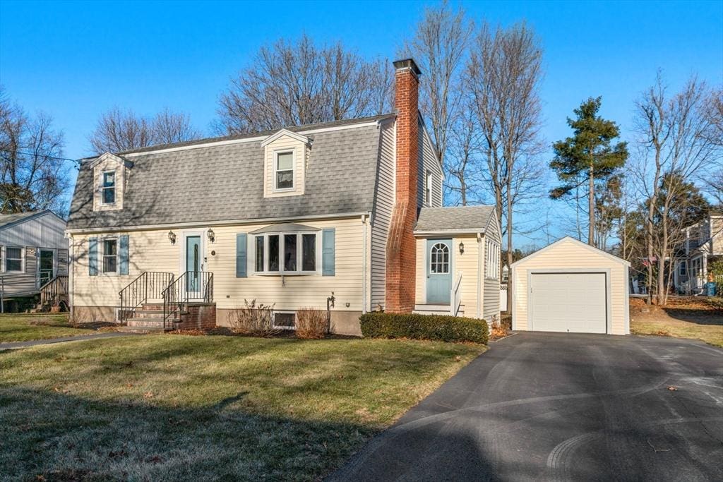 cape cod home with a garage, a front yard, and an outbuilding