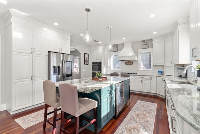 kitchen featuring a center island, sink, custom exhaust hood, white cabinetry, and appliances with stainless steel finishes