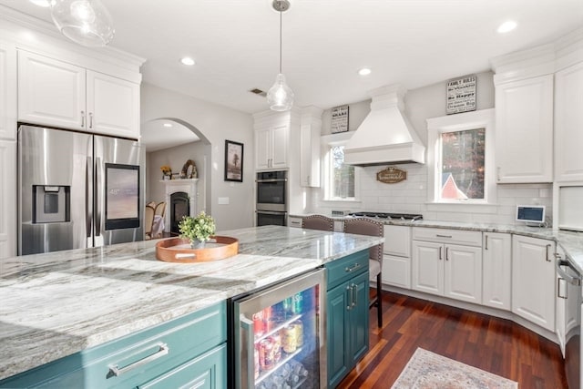 kitchen with white cabinetry, blue cabinetry, appliances with stainless steel finishes, and premium range hood