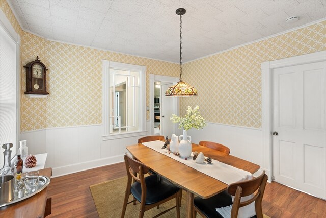 dining room featuring crown molding, dark wood-style flooring, wallpapered walls, and wainscoting