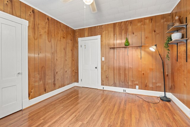 empty room with a ceiling fan, baseboards, wood walls, and wood finished floors