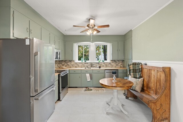 kitchen with green cabinetry, appliances with stainless steel finishes, a sink, a ceiling fan, and backsplash
