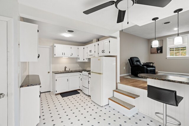 kitchen featuring visible vents, dark countertops, a sink, white cabinets, and white appliances