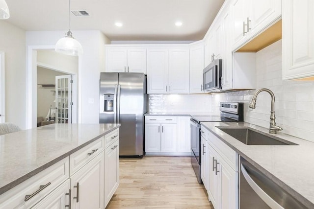 kitchen with appliances with stainless steel finishes, sink, white cabinets, hanging light fixtures, and light hardwood / wood-style flooring