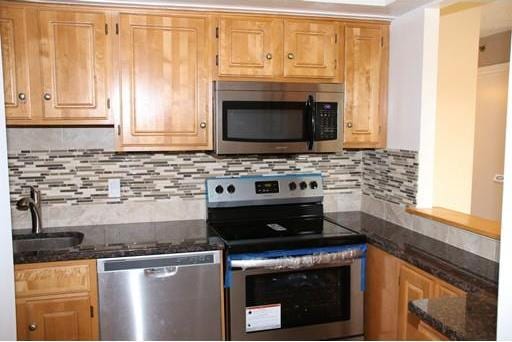 kitchen featuring dark stone counters, tasteful backsplash, appliances with stainless steel finishes, and sink