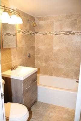 full bathroom with toilet, tiled shower / bath combo, vanity, tile walls, and tile floors