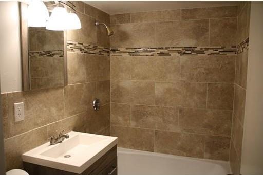 full bathroom with tile walls, tiled shower / bath combo, tasteful backsplash, toilet, and vanity