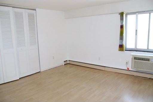 unfurnished bedroom with a closet, light wood-type flooring, an AC wall unit, and a baseboard heating unit