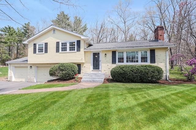 split level home featuring a chimney, a front yard, a garage, brick siding, and aphalt driveway
