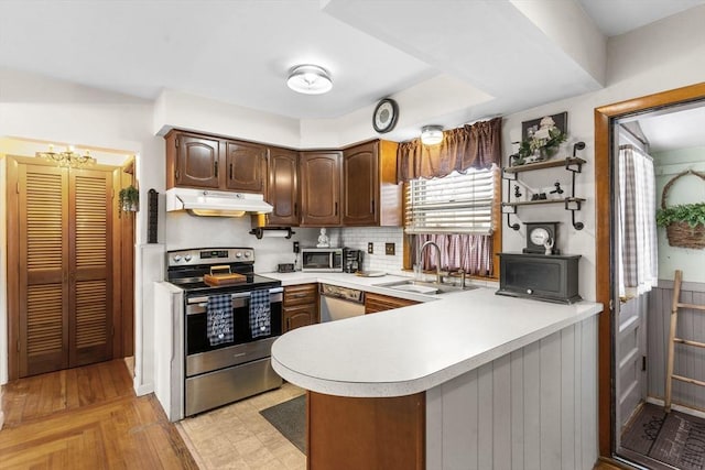 kitchen with under cabinet range hood, a sink, appliances with stainless steel finishes, a peninsula, and light countertops