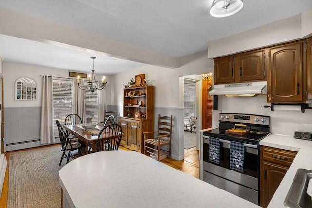 kitchen with under cabinet range hood, a wainscoted wall, light countertops, stainless steel electric range, and an inviting chandelier