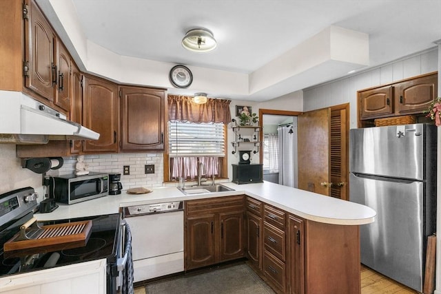 kitchen with under cabinet range hood, a sink, appliances with stainless steel finishes, a peninsula, and light countertops